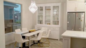 Een moderne keuken met witte kasten, een kroonluchter, en een eethoek met witte stoelen en een tafel.