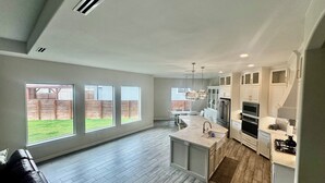 Een moderne keuken met een groot eiland, witte kasten en uitzicht op een achtertuin door grote ramen.