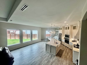 A modern kitchen with a large island, white cabinetry, and a view of a backyard through large windows.