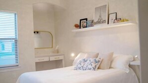 Een slaapkamer met een bed, nachtkastje, spiegel en een plank met foto’s.
