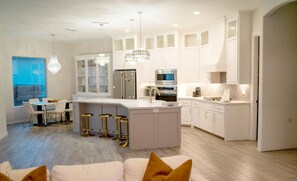 A modern kitchen with white cabinetry, a central island, bar stools, and pendant lighting.