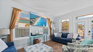 Ein Wohnzimmer mit einem großen Fernseher, einem Sofa, einem Couchtisch und Blick auf den Strand durch die Fenster.