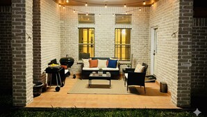An enclosed patio with a brick wall, a black grill, a sofa, and a dining table. - Tropical Family Funhouse, Relax: No Chore Pet friendly Rental (Edinburg)