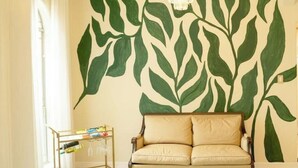 A room with a large wall mural of green leaves, a sofa, and a small table with items on it. - Tropical Family Funhouse, Relax: No Chore Pet friendly Rental (Edinburg)