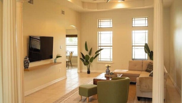 A spacious living room with a flat-screen TV, a sofa, a coffee table, and a ceiling fan. - Tropical Family Funhouse, Relax: No Chore Pet friendly Rental (Edinburg)