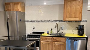 A modern kitchen with wooden cabinets, stainless steel appliances, a yellow countertop, and a dishwasher. - Beautiful Girdwood Condo (Anchorage)