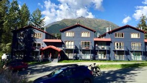 A row of blue buildings with red roofs, likely a hotel or guesthouse, with a mountain in the background. - Beautiful Girdwood Condo (Anchorage)
