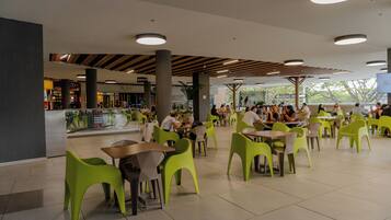 A spacious indoor dining area with high tables and bright green chairs, surrounded by pillars and large windows.