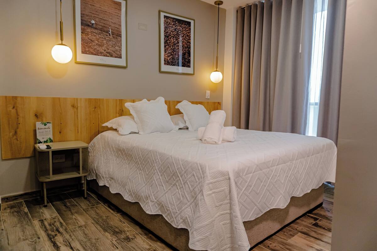 A neatly made bed with a white bedspread, a wooden headboard, and two wall-mounted light fixtures.
