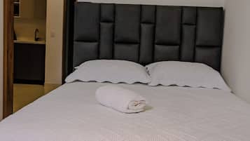Una cama bien tendida con cabecera oscura, ropa de cama blanca y una toalla enrollada sobre la cama.