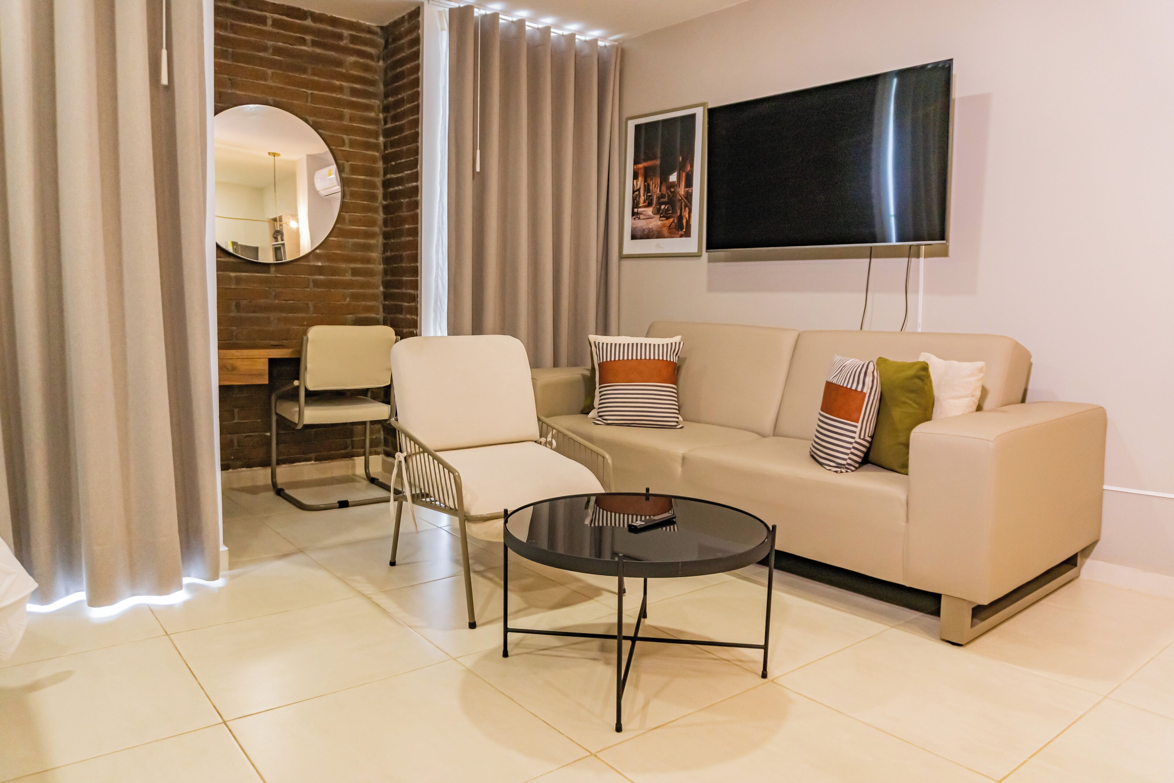 A modern living room with a sofa, armchairs, a coffee table, a flat-screen TV, and a brick accent wall.