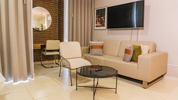 Una sala de estar moderna con un sofá, sillones, una mesa de centro, un televisor de pantalla plana y una pared de ladrillo decorativa.