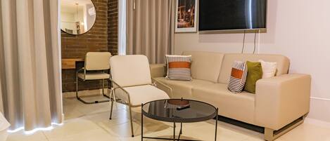 A modern living room with a sofa, armchairs, a coffee table, a flat-screen TV, and a brick accent wall.