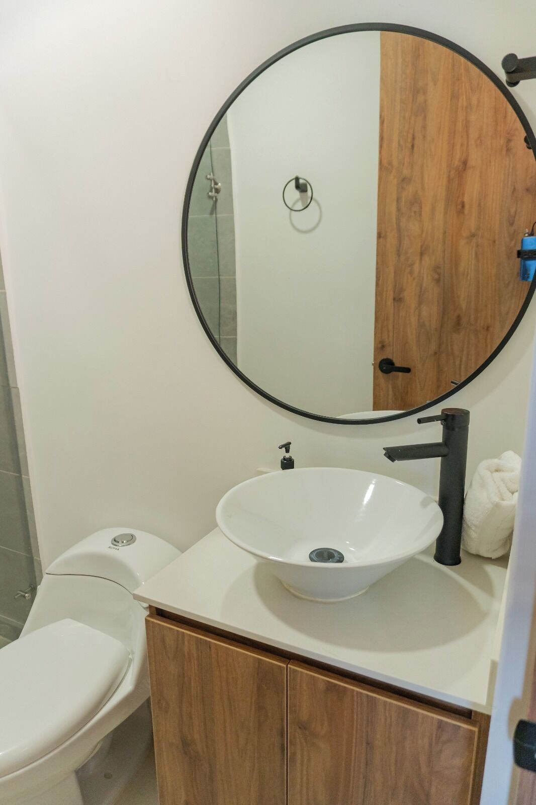 Une salle de bain avec un lavabo blanc, un miroir rond et un meuble en bois.