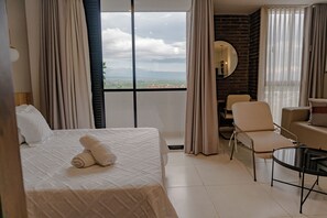 Habitación de hotel con cama, una silla, una mesita, un espejo y vistas a la ciudad.