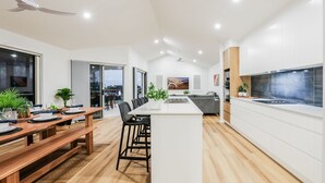 A modern kitchen with a central island, a dining area with a wooden table, and a view of the cityscape through large windows.