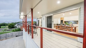 A spacious balcony with a wooden railing, a dining area with a wooden table and chairs, and a view of the surrounding landscape.