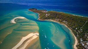 Vista aérea de una zona costera con aguas turquesas cristalinas, playas de arena y una pequeña isla con edificios.