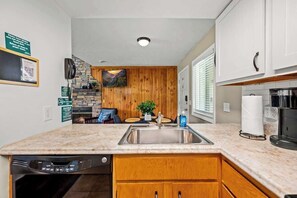 A compact kitchen with a granite countertop, wooden cabinets, a built-in dishwasher, and a stone backsplash.