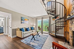 A spacious living room with a beige sofa, a coffee table, and a view of a balcony. - Mountain Views | Indoor Pool & Hot Tub Access (Gatlinburg)