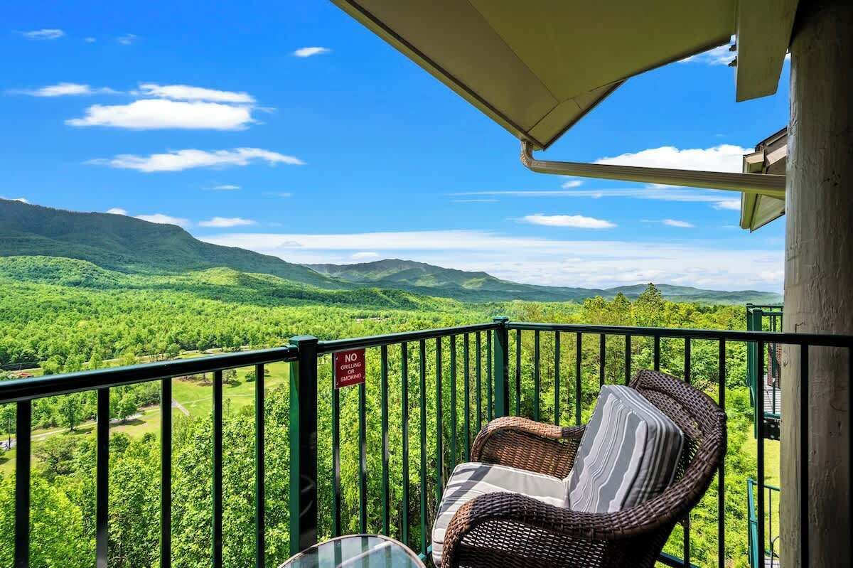 A balcony with wicker furniture overlooking a lush green landscape and mountains.