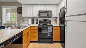 A modern kitchen with white cabinets, a black stove, a microwave, and a refrigerator. - Mountain Views | Indoor Pool & Hot Tub Access (Gatlinburg)