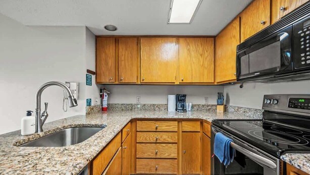 Una cocina con encimeras de granito, gabinetes de madera y electrodomésticos de acero inoxidable, incluyendo un horno empotrado.