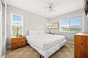 A bedroom with a bed, two bedside tables, a nightstand, a ceiling fan, and two windows with blinds.