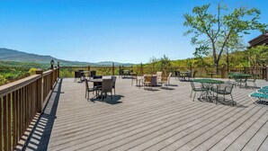 Eine Holzterrasse mit Gartenmöbeln, darunter Tische und Stühle, mit Blick auf eine Berglandschaft.