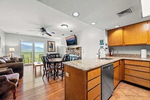 Uma sala de estar espaçosa com uma mesa de jantar e cadeiras, uma cozinha com armários de madeira e bancadas de granito, e um ventilador de teto.
