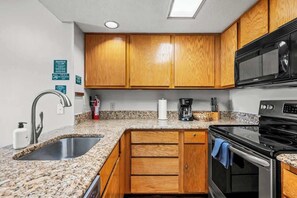 Una cocina con encimeras de granito, armarios de madera y electrodomésticos de acero inoxidable, incluyendo un microondas.