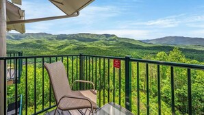 A balcony with a chair and a table, overlooking a mountainous landscape.