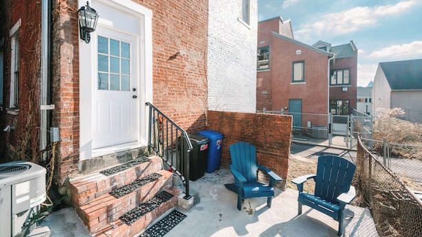 A residential building with a white door, brick walls, and a small outdoor area with steps leading to the door.