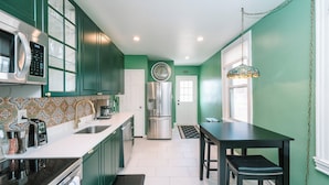 A kitchen with green cabinets, a stainless steel refrigerator, a microwave, and a dining table with chairs.