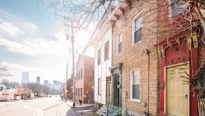 A street view with a row of brick buildings, a yellow door, and a city skyline in the background.