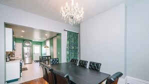 A dining area with a dark wooden table and leather chairs, a chandelier, and a view into the kitchen.