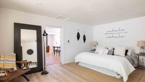 A bedroom with a large bed, a wooden rocking chair, a mirror, and a wall with the words "inhale exhale" written on it.
