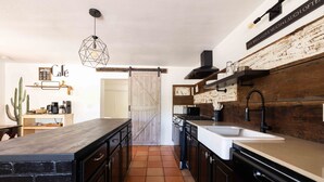 A kitchen with dark cabinetry, a large island, a hanging light fixture, and a rustic wall.