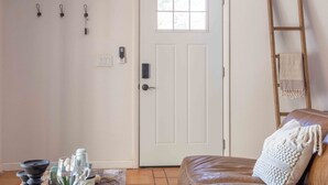A living room with a brown leather couch, a wooden coffee table with decorative items, a white door with a window, and a wooden ladder leaning against the wall.