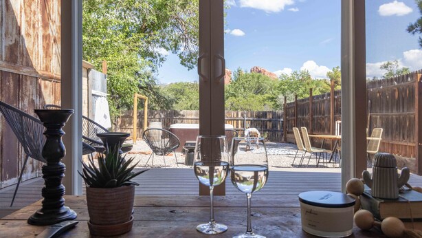 An outdoor patio with a wooden deck, potted plants, two wine glasses, a candle, and a rustic fence in the background.