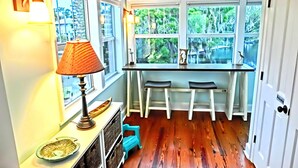 A kitchen with a wooden floor, a table with chairs, a lamp, and a view of trees through the windows. - Swim Mat, Kayaks, Fire Pit! PET FRIENDLY - Sunfish Cove - Weeki Wachee River (Weeki Wachee)