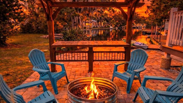 A fire pit with four Adirondack chairs arranged around it, set on a brick patio with a wooden pergola overhead. - Swim Mat, Kayaks, Fire Pit! PET FRIENDLY - Sunfish Cove - Weeki Wachee River (Weeki Wachee)