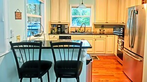 A kitchen with white cabinets, a stainless steel refrigerator, and a dining area with two chairs. - Swim Mat, Kayaks, Fire Pit! PET FRIENDLY - Sunfish Cove - Weeki Wachee River (Weeki Wachee)