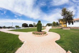 Un camino de ladrillo circular que conduce a una escultura verde central rodeada de flores.