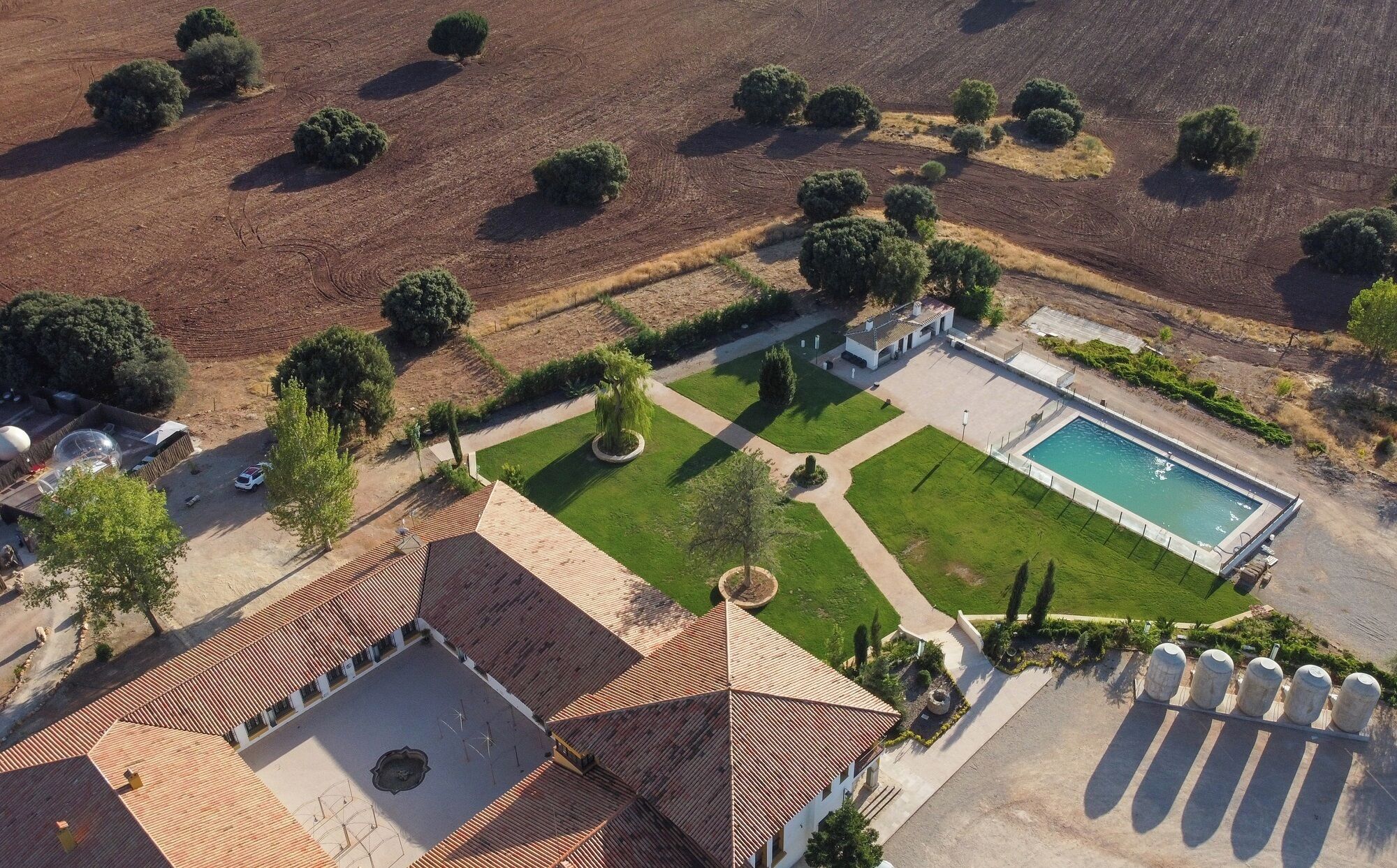 Vue aérienne d’une propriété dotée d’une piscine, d’un court de tennis et d’un jardin aménagé.