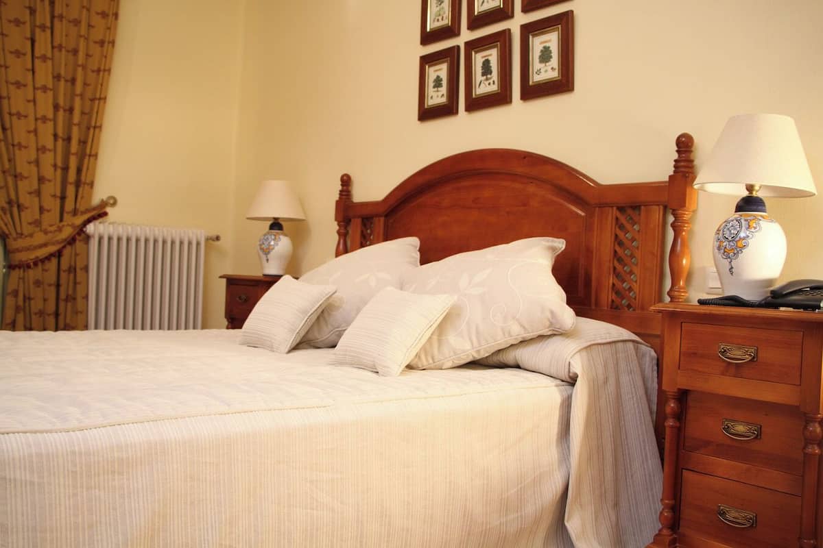 Un lit bien fait, avec une tête de lit en bois, deux tables de chevet avec des lampes et un radiateur en arrière-plan.