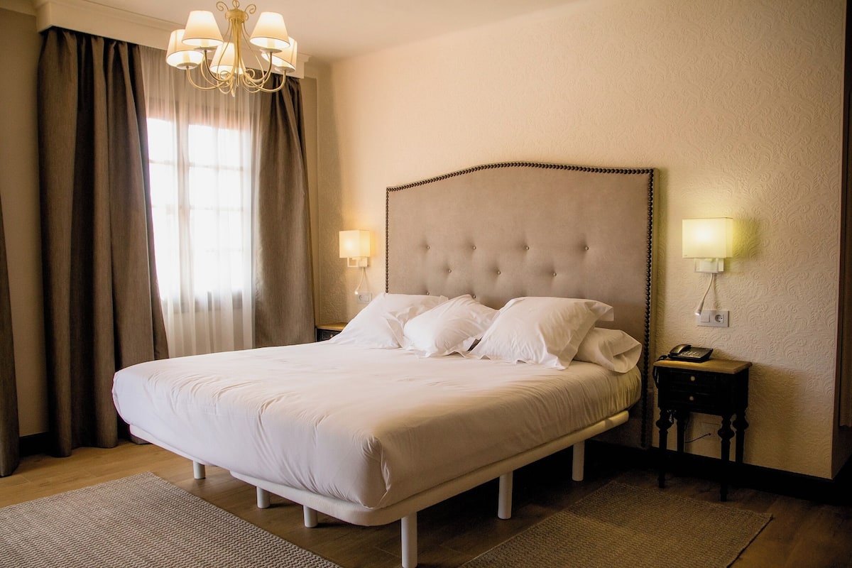 Un lit bien fait, avec du linge de lit blanc, une tête de lit capitonnée, des lampes de chevet et une petite table de chevet avec une lampe.