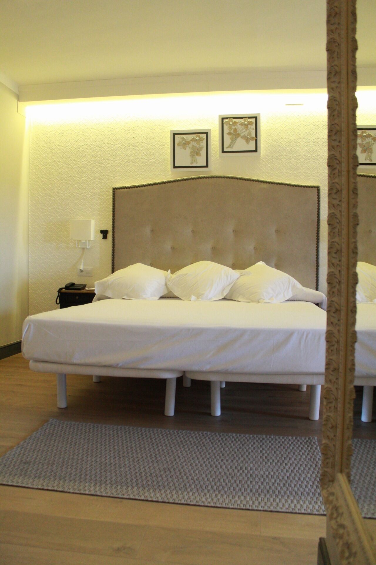 Un lit double avec une tête de lit capitonnée, du linge de lit blanc et une petite table de chevet avec une lampe.
