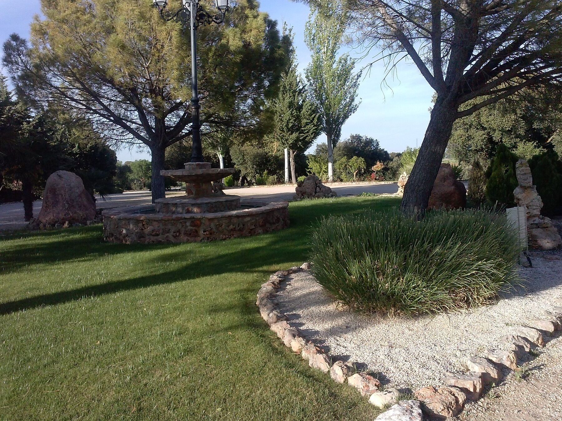 Un jardín con una fuente de piedra, rocas grandes y un césped bien cuidado.