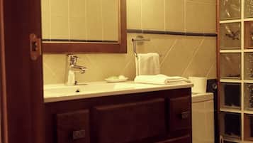 Un baño con lavamanos blanco, espejo, toallero y cabina de ducha de vidrio.
